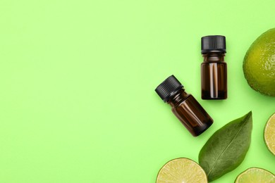 Photo of Bottles of citrus essential oil and fresh limes on green background, flat lay. Space for text