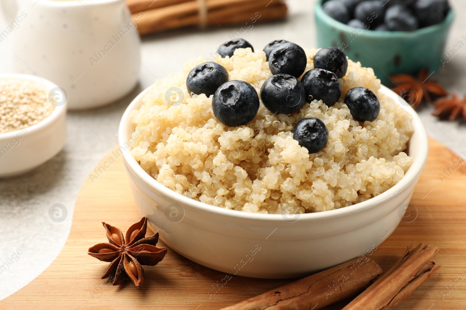 Photo of Tasty quinoa porridge with blueberries in bowl and spices on table, closeup