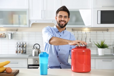Young man preparing protein shake at table in kitchen