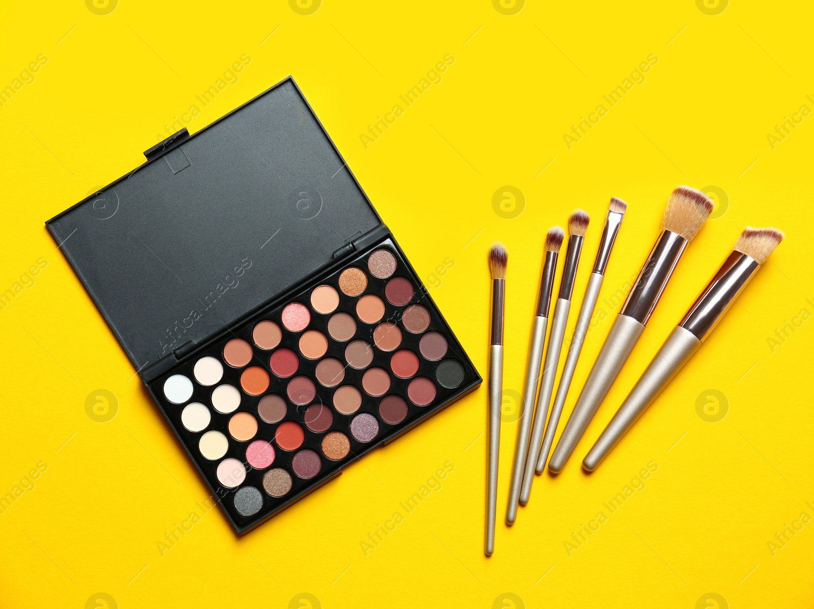 Photo of Flat lay composition with professional makeup brushes and eye shadow palette on yellow background