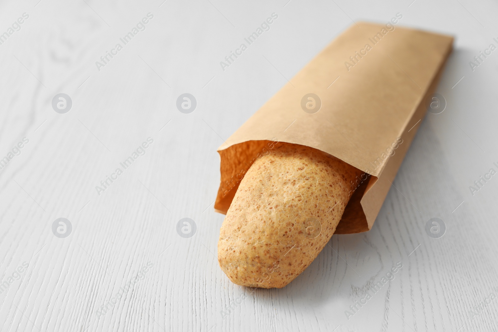 Photo of Baguette in paper bag on wooden table. Space for text