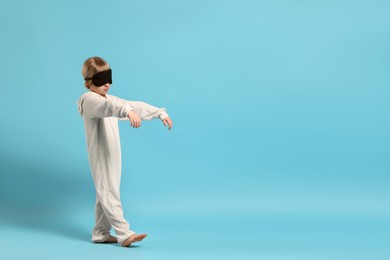 Boy in pajamas and sleep mask sleepwalking on light blue background, space for text