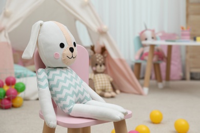 Photo of Cute toy bunny on small chair in playroom. Interior design