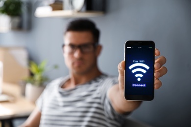 Image of Man connecting to WiFi using mobile phone indoors, focus on device