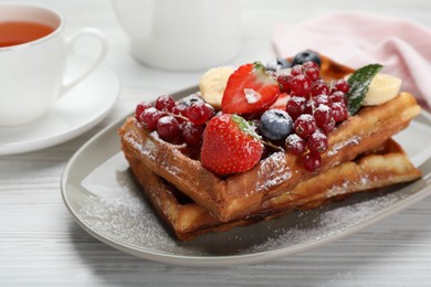 Photo of Plate of delicious Belgian waffles with berries and powdered sugar on white wooden table, closeup
