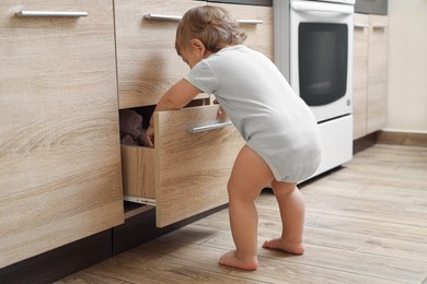 Little child exploring drawer in kitchen. Dangerous situation