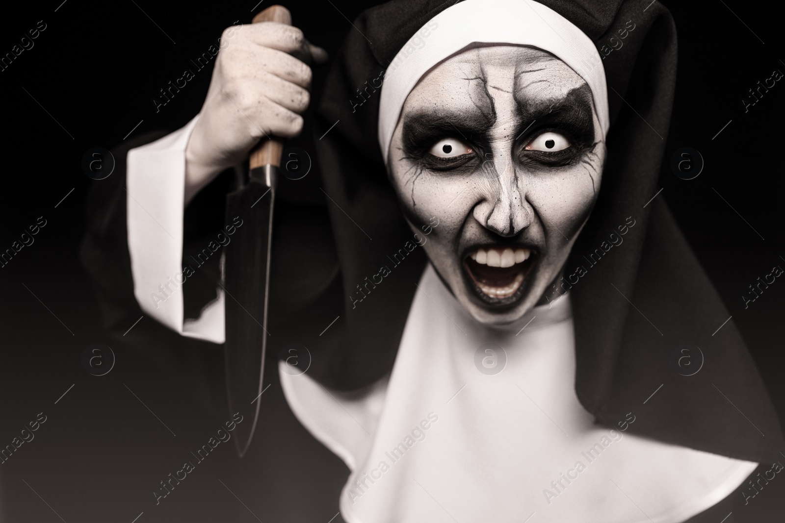 Photo of Scary devilish nun with knife on black background. Halloween party look