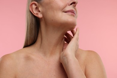 Mature woman touching her neck on pink background, closeup