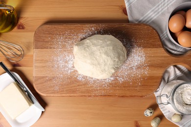 Fresh dough sprinkled with flour and other ingredients on wooden table, flat lay