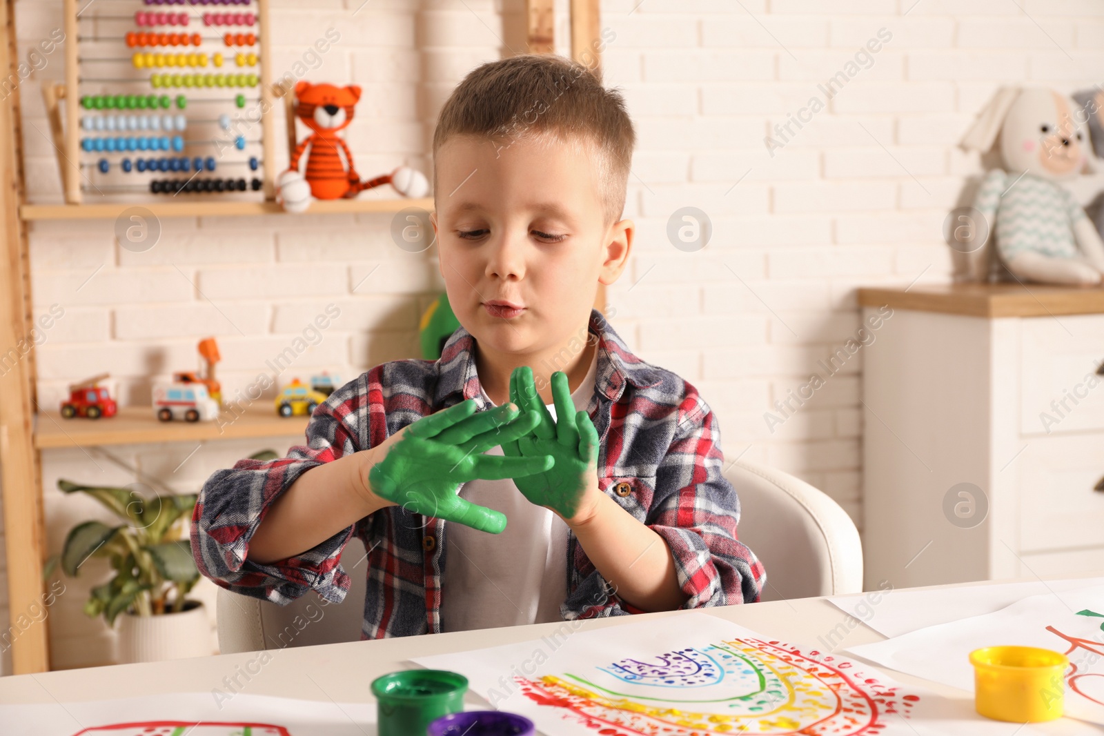 Photo of Little boy showing painted palms at white table indoors