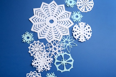 Photo of Many paper snowflakes on blue background, flat lay
