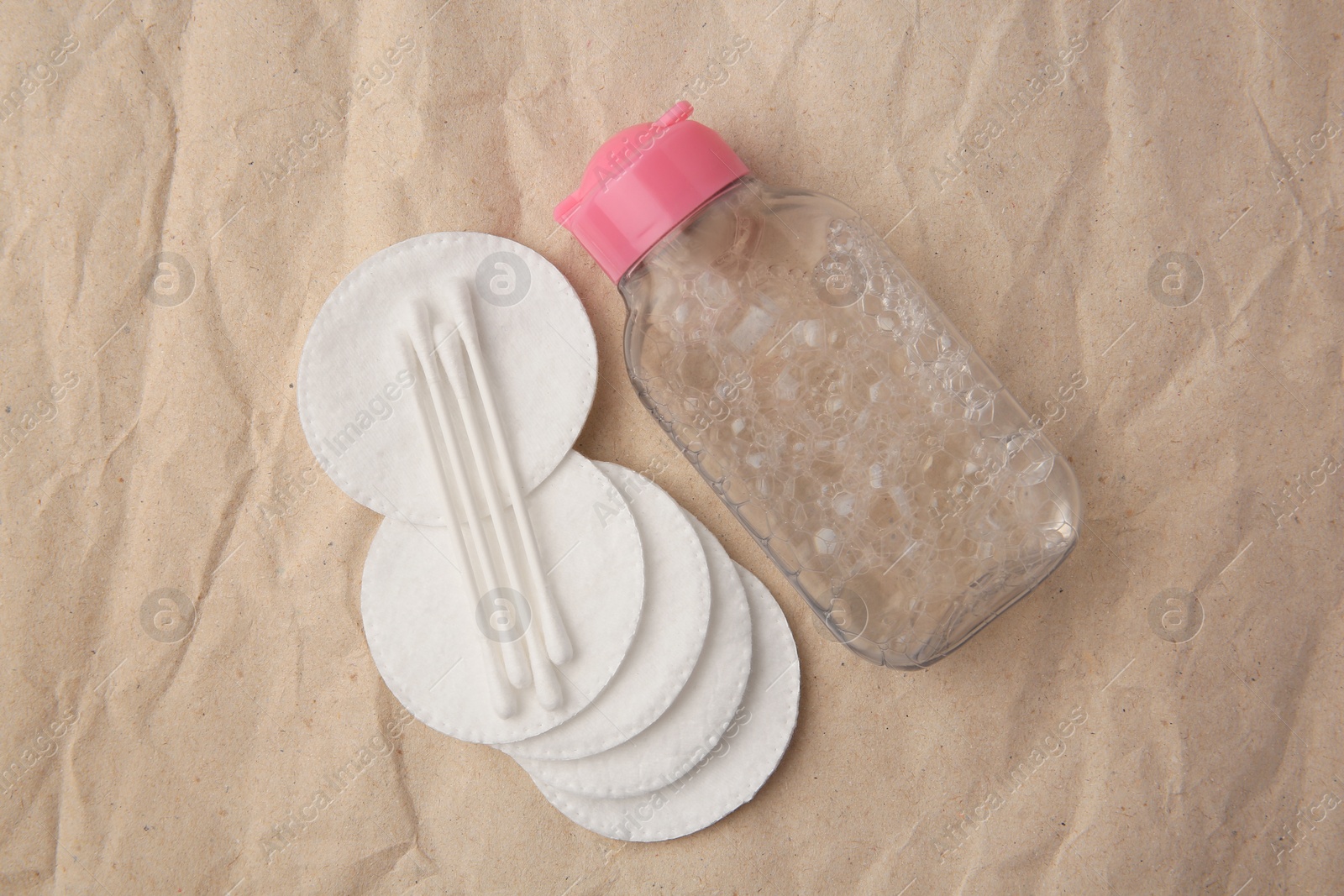 Photo of Makeup remover, cotton swabs and pads on crumpled paper, flat lay