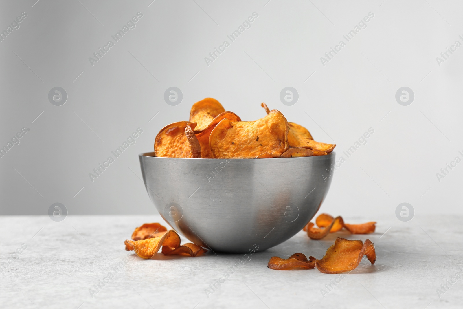 Photo of Bowl and sweet potato chips on table against light background