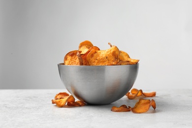 Photo of Bowl and sweet potato chips on table against light background