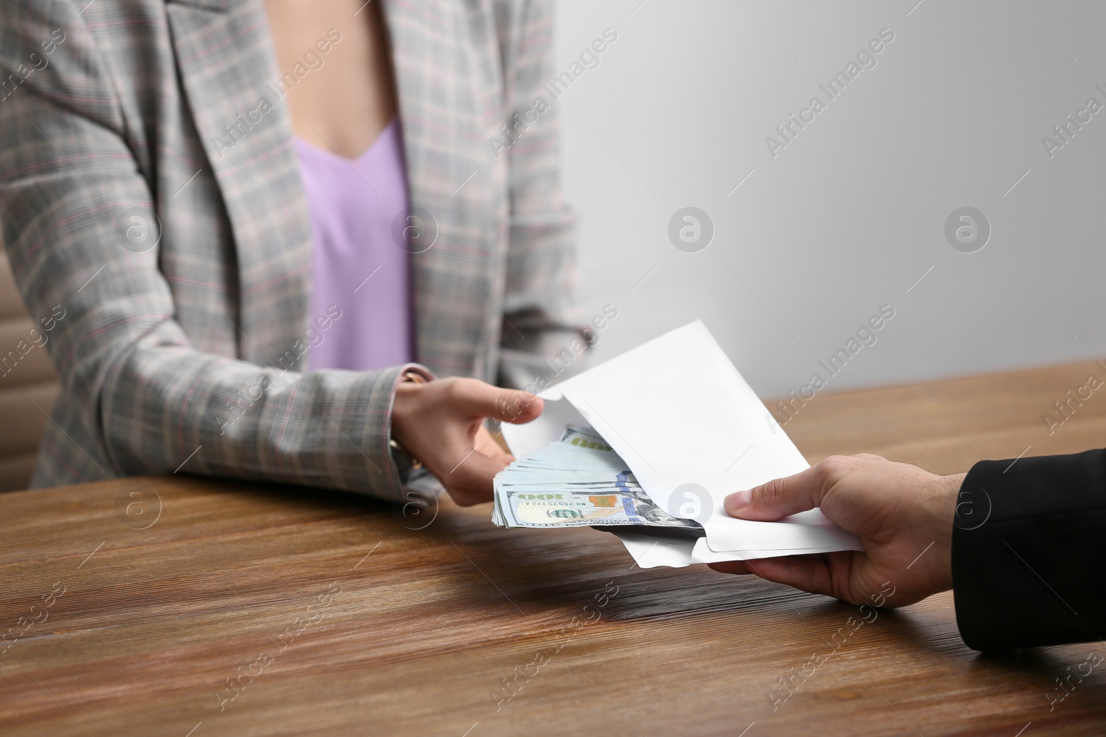 Photo of Man giving bribe money to woman at table indoors, closeup