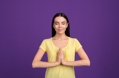 Young woman meditating on purple background. Stress relief exercise