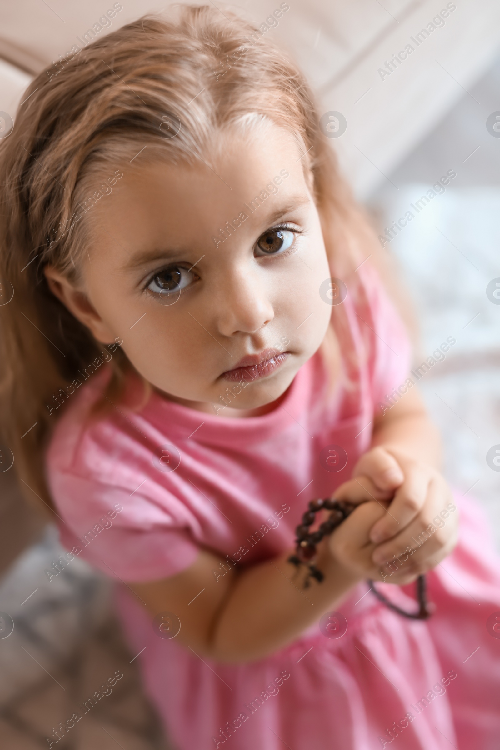 Photo of Cute little girl with beads praying on blurred background