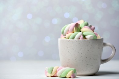 Ceramic cup with colorful marshmallows on white table against blurred lights. Space for text