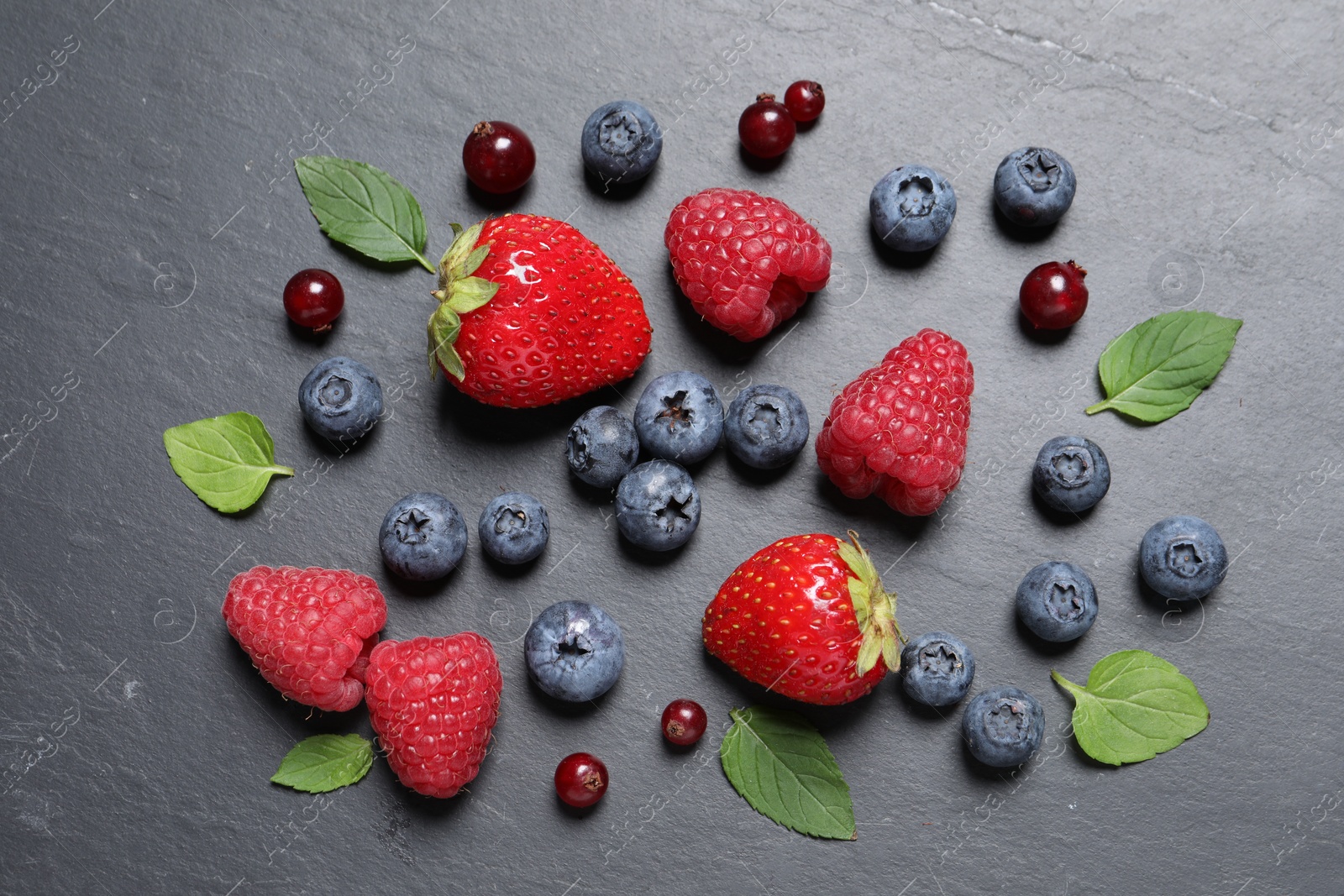 Photo of Many different fresh ripe berries and green leaves on dark grey table, flat lay