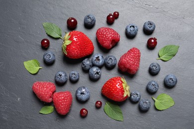 Many different fresh ripe berries and green leaves on dark grey table, flat lay