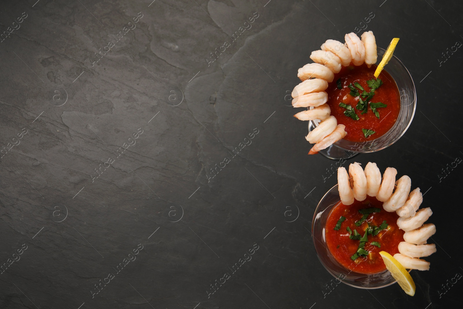 Photo of Tasty shrimp cocktail with sauce in glasses and lemon on grey textured table, flat lay. Space for text