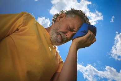 Photo of Senior man with cold pack suffering from heat stroke outdoors, low angle view