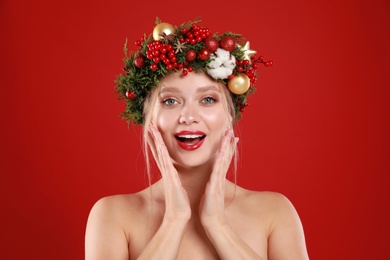 Beautiful young woman wearing Christmas wreath on red background