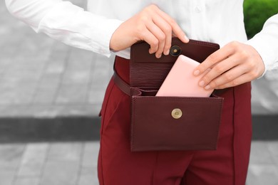 Woman taking cosmetic pocket mirror from bag outdoors, closeup. Space for text