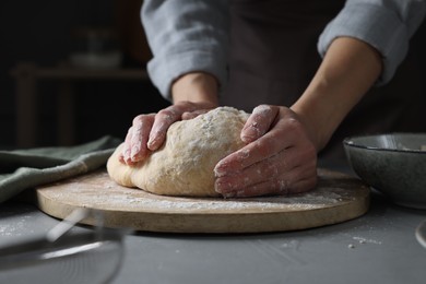 Photo of Woman kneading dough at grey table, closeup