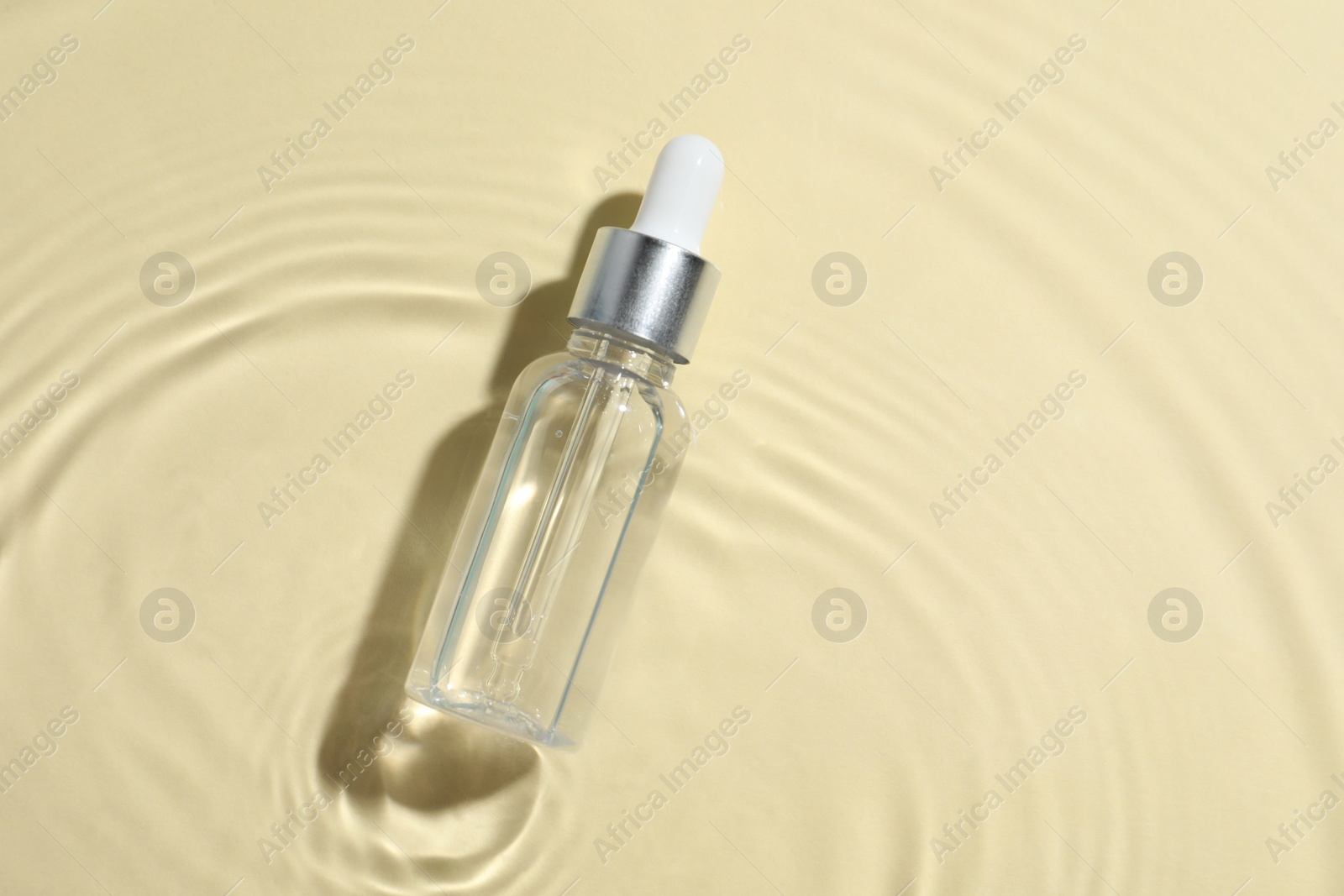 Photo of Bottle of cosmetic oil in water on beige background, top view. Space for text