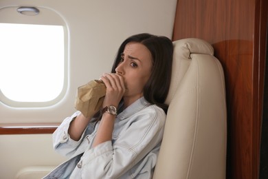 Photo of Nervous young woman with aviophobia breathing into paper bag in airplane