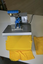 Photo of Printing logo. Heat press with yellow t-shirts on white table