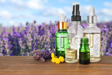 Image of Bottles of essential oils and wildflowers on wooden table against blurred background. Space for text