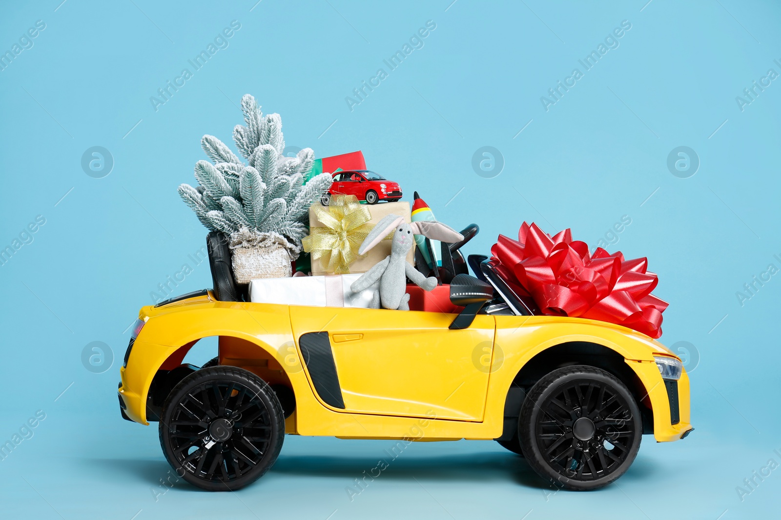 Photo of Child's electric car with toys, gift boxes and Christmas decor on light blue background