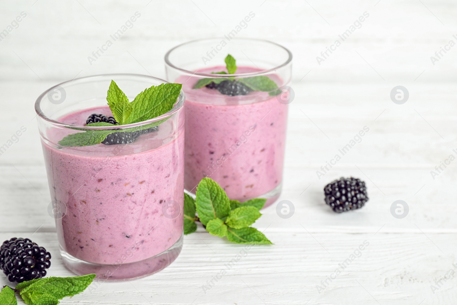 Photo of Delicious blackberry smoothie in glasses on white table, space for text