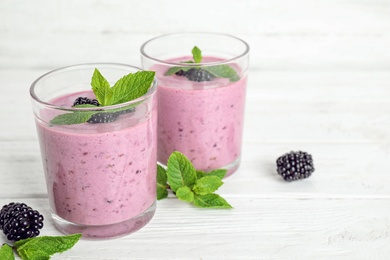 Delicious blackberry smoothie in glasses on white table, space for text