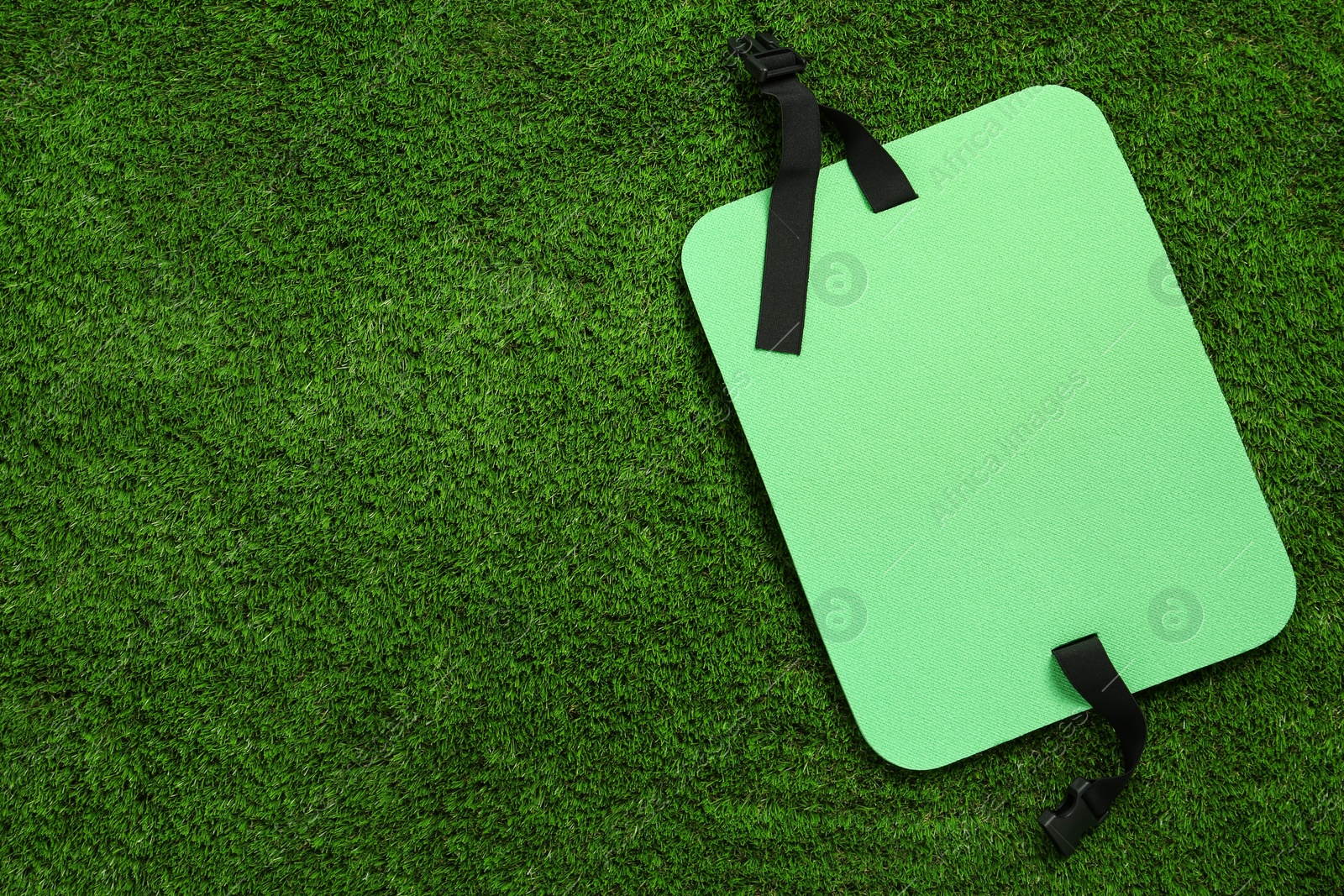 Photo of Bright foam tourist seat mat on green grass, top view. Space for text
