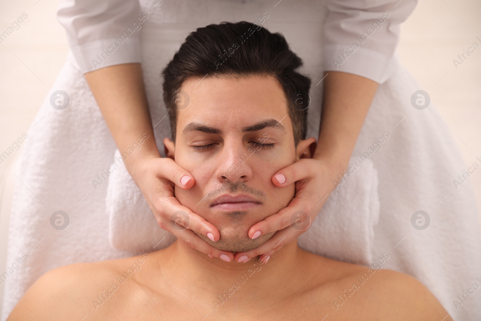 Photo of Man receiving facial massage in beauty salon, top view