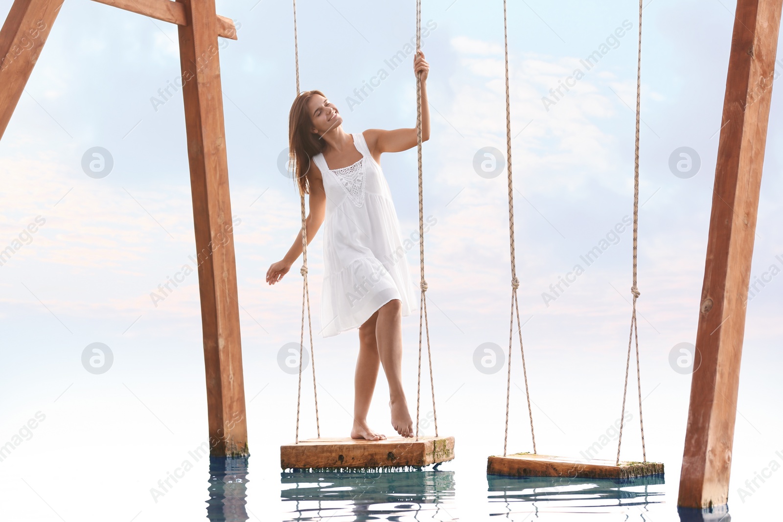 Photo of Young woman enjoying sunrise on swing over water