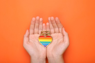 Photo of Woman holding rainbow heart shaped pendant on orange background, top view. LGBT pride