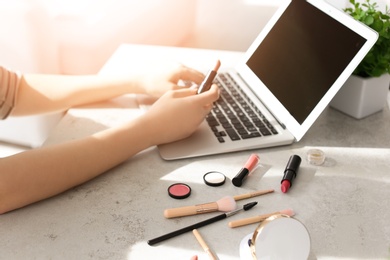 Photo of Young woman with makeup products using laptop at table. Beauty blogger