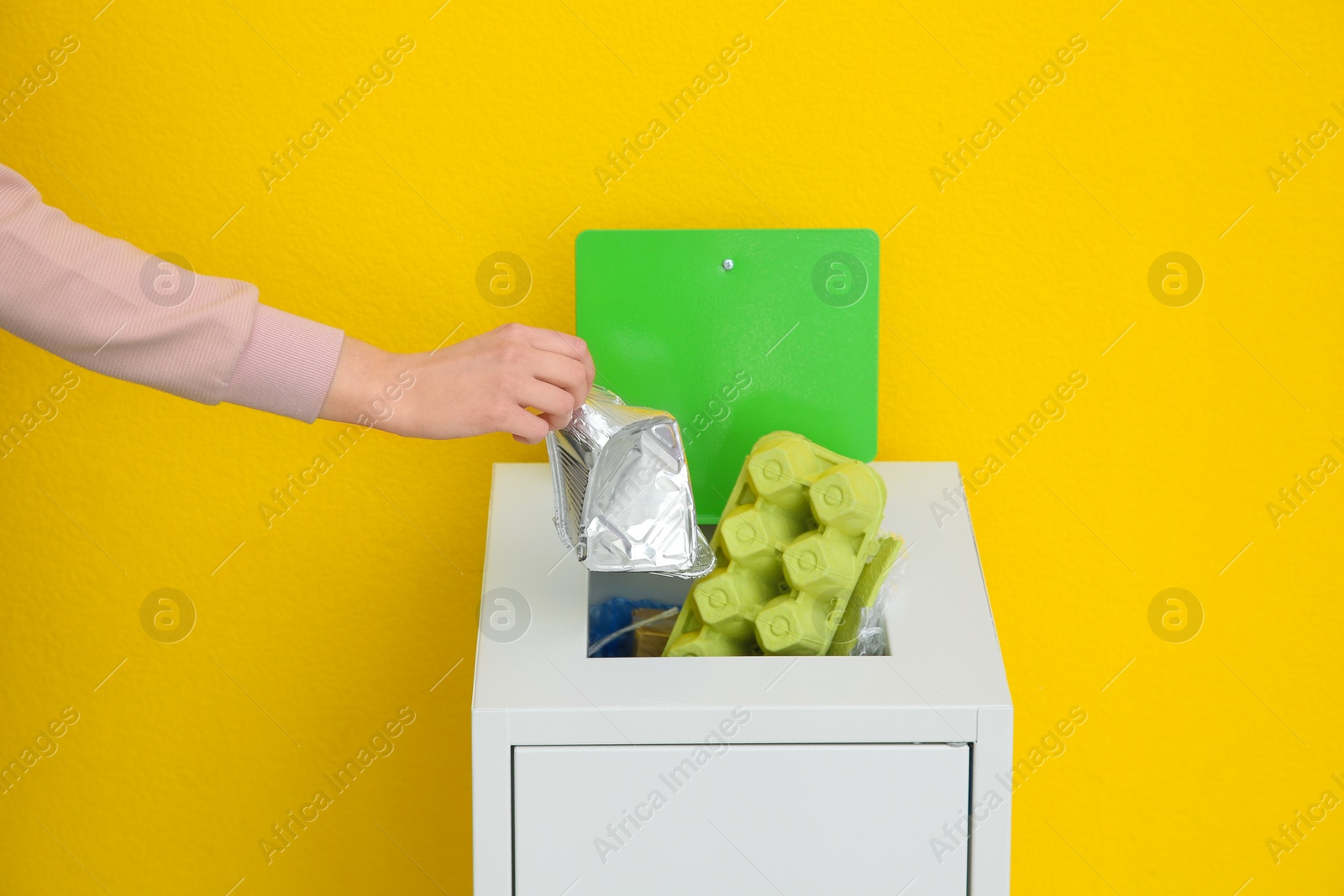 Photo of Woman putting used foil container into trash bin on color background, closeup. Recycling concept