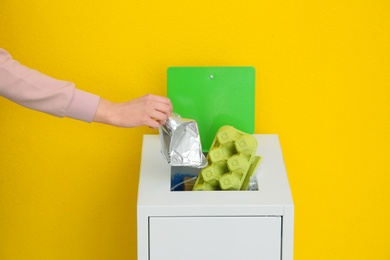 Woman putting used foil container into trash bin on color background, closeup. Recycling concept