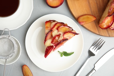 Photo of Slice of delicious cake with plums on light table, flat lay
