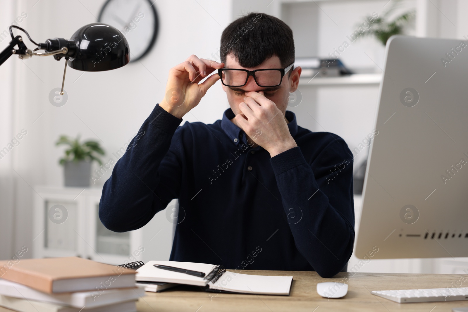 Photo of Young man suffering from headache at workplace in office