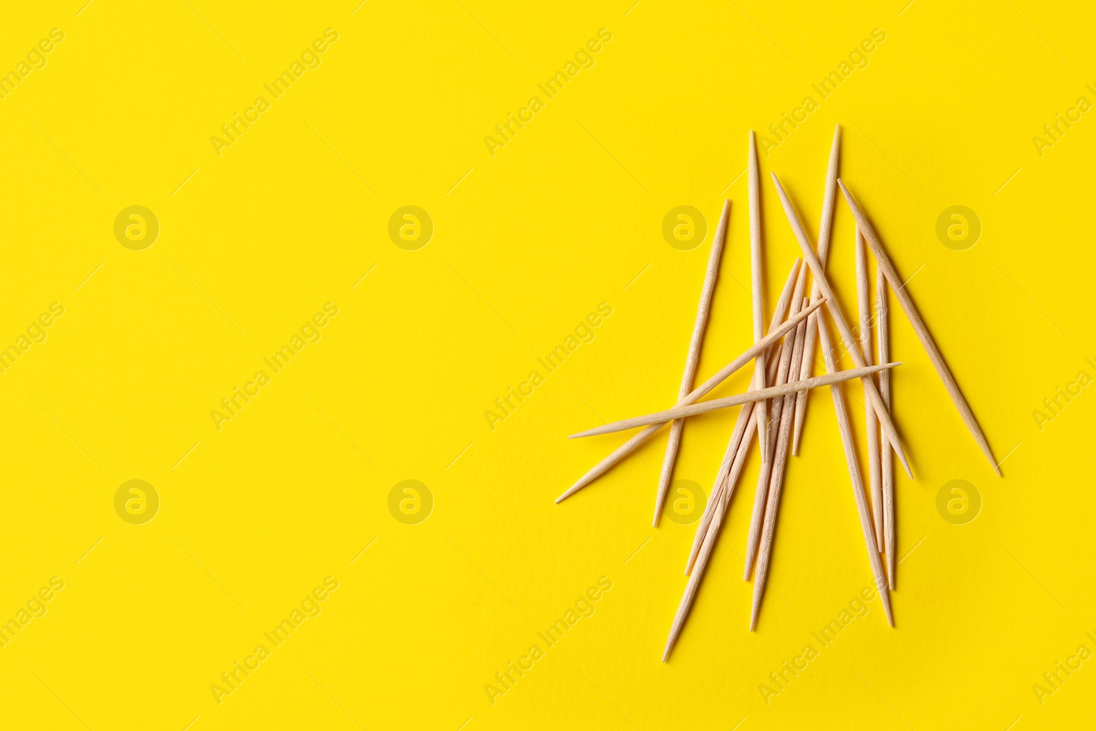 Photo of Wooden toothpicks on yellow background, flat lay. Space for text