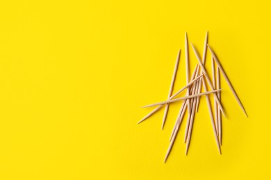 Wooden toothpicks on yellow background, flat lay. Space for text