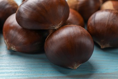 Photo of Roasted edible sweet chestnuts on light blue wooden table, closeup