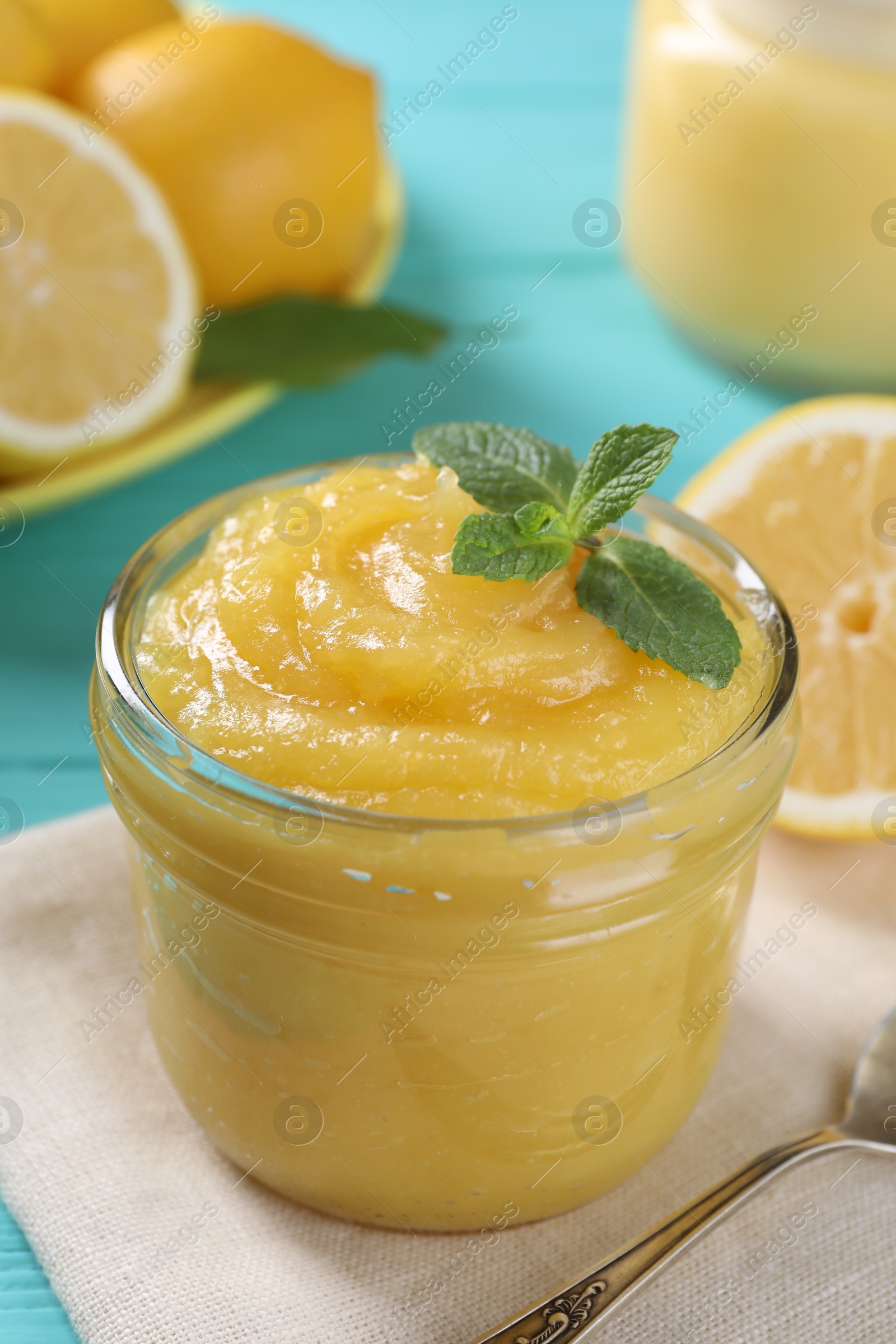 Photo of Delicious lemon curd in glass jar, fresh citrus fruits, mint and spoon on light blue table, closeup