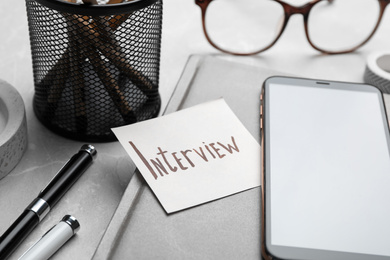 Photo of Reminder note about job interview and stationery on table, closeup